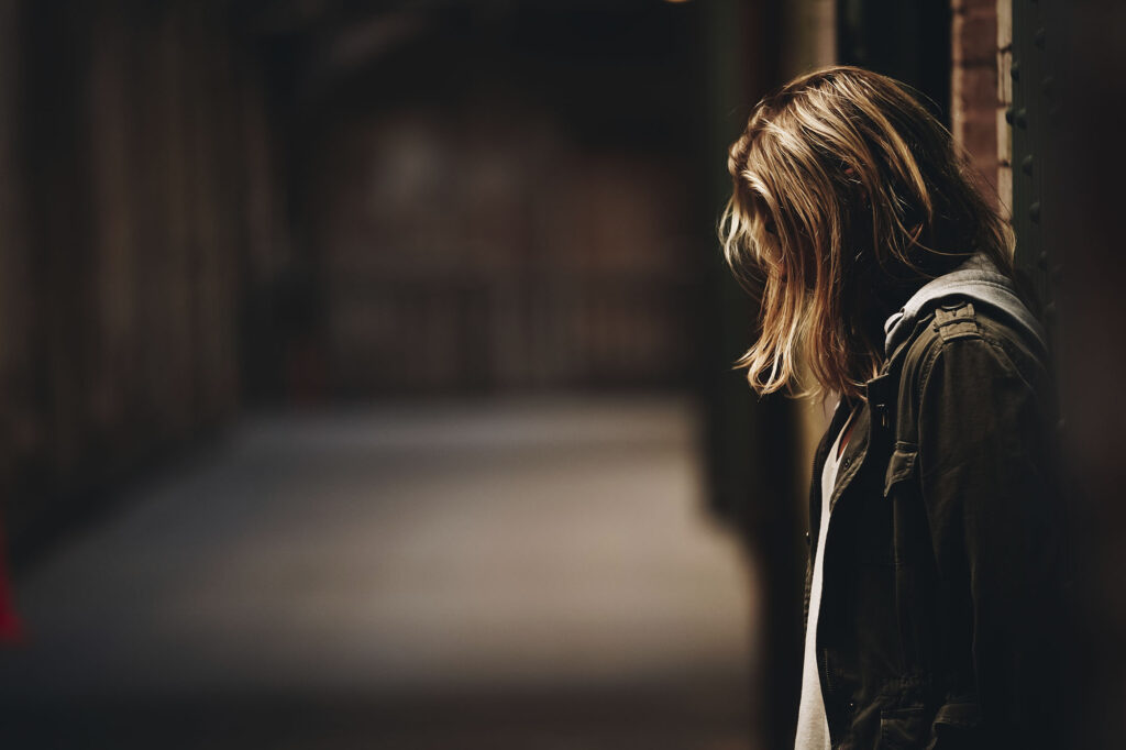 A female leaning against the wall looking down in a hallway